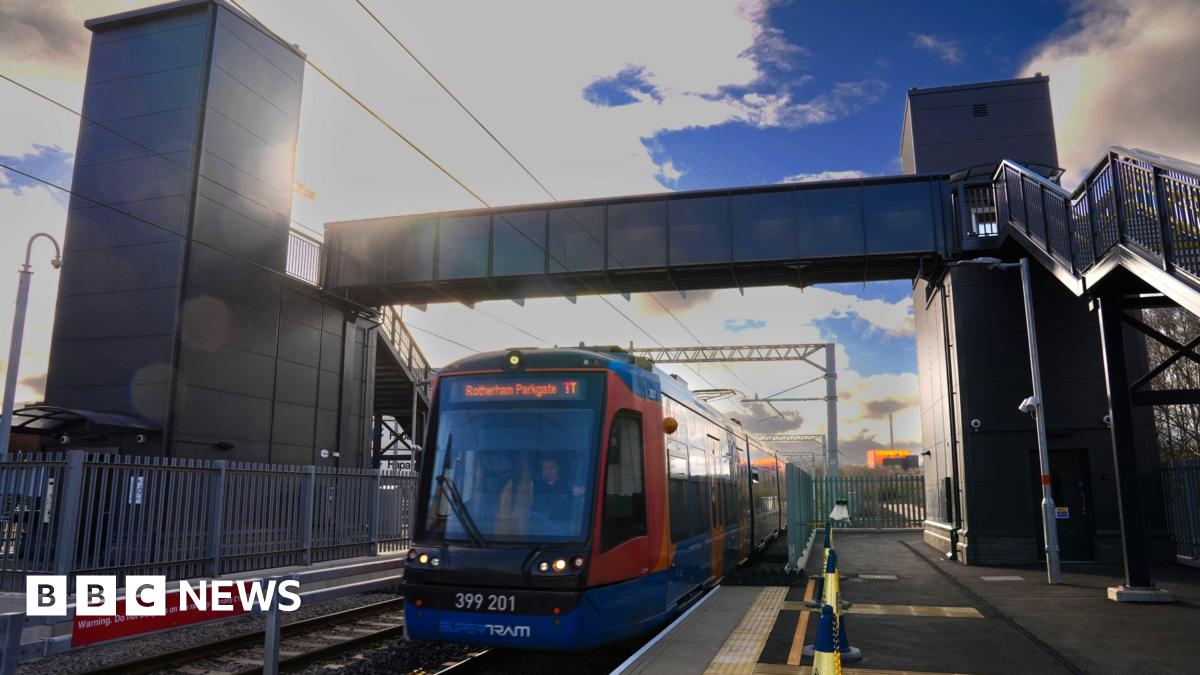 A red and blue Supertram is driving on the tracks under a metal pedestrian bridge