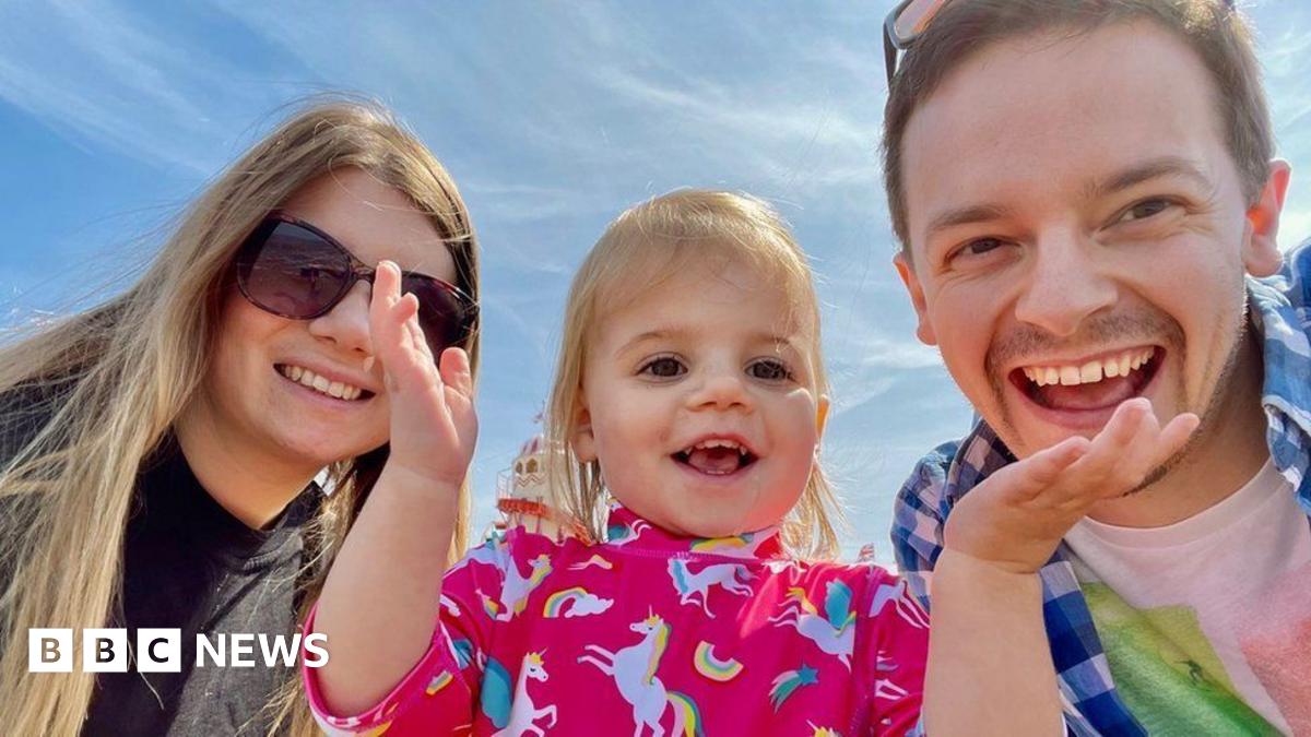 Rebecca Ableman smiling to the camera in a dark navy knitted jumper - there is a beautiful walled garden behind her