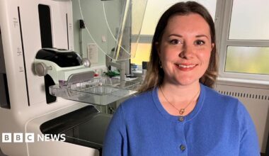 Rebecca Corbett, Quality and Improvement Manager for West Sussex Brighton and Hove Breast screening Service. Rebecca, who is sat in front of the screening machine, is wearing a blue t-shirt and has her hair down.