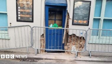 The entrance to the pub fenced off, with the wall and door damaged.