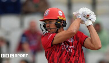 Chris Green wearing Lancashire's red T20 kit, plays a big shot while batting with his gloves and helmet on