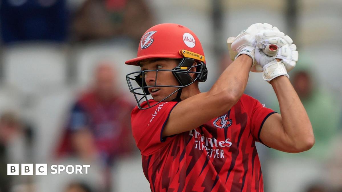 Chris Green wearing Lancashire's red T20 kit, plays a big shot while batting with his gloves and helmet on