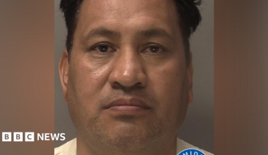 A police mugshot of a man with dark hair. He is wearing a cream jumper. There is a West Midlands Police logo in the bottom right corner.