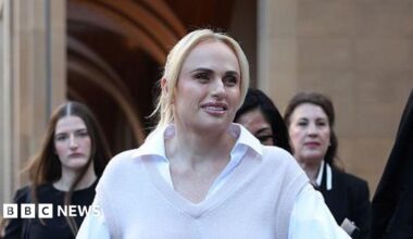 A woman with blonde hair, wearing a white shirt and beige vest