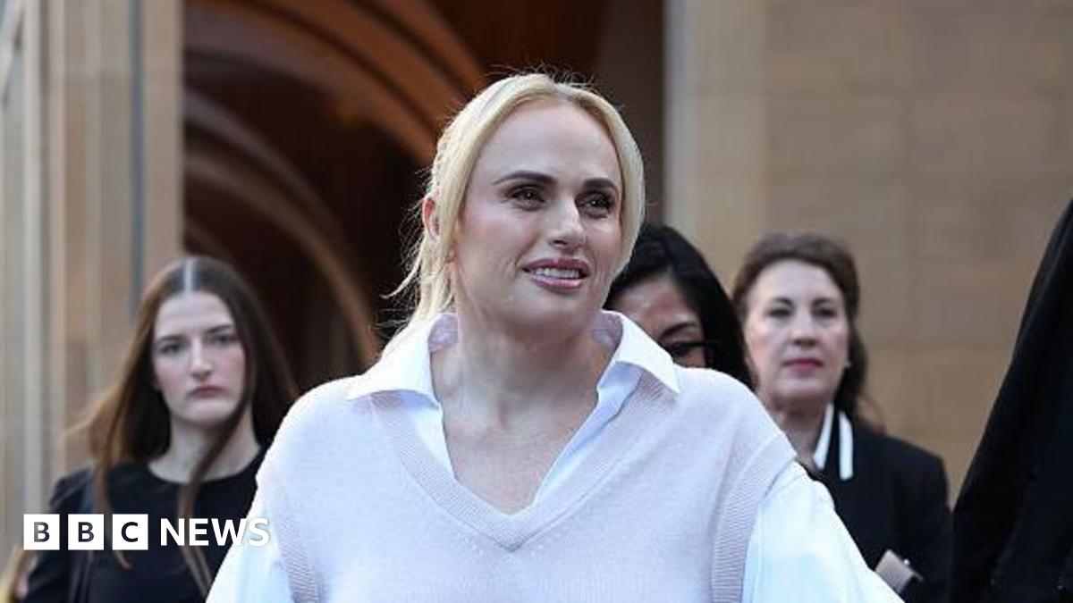 A woman with blonde hair, wearing a white shirt and beige vest