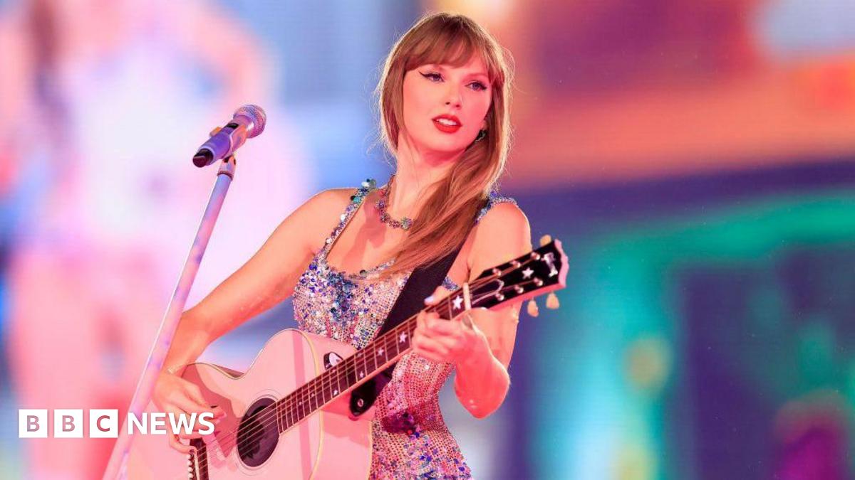 Taylor Swift on stage playing a pink guitar in a sparkly top