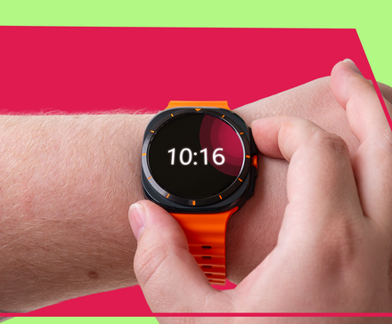 Close-up of a hand pressing the side button on a Samsung Galaxy Watch displaying a simple digital clock face.