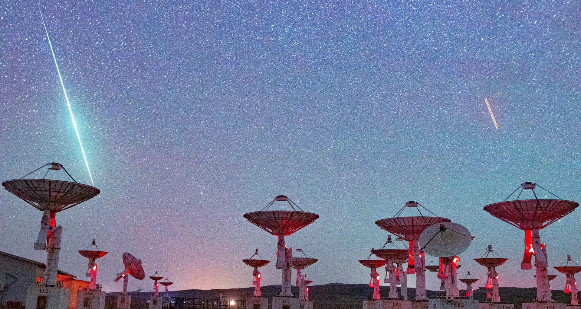 Shooting stars are pictured streaking towards a collection of radar dishes pointing towards the starry night sky.