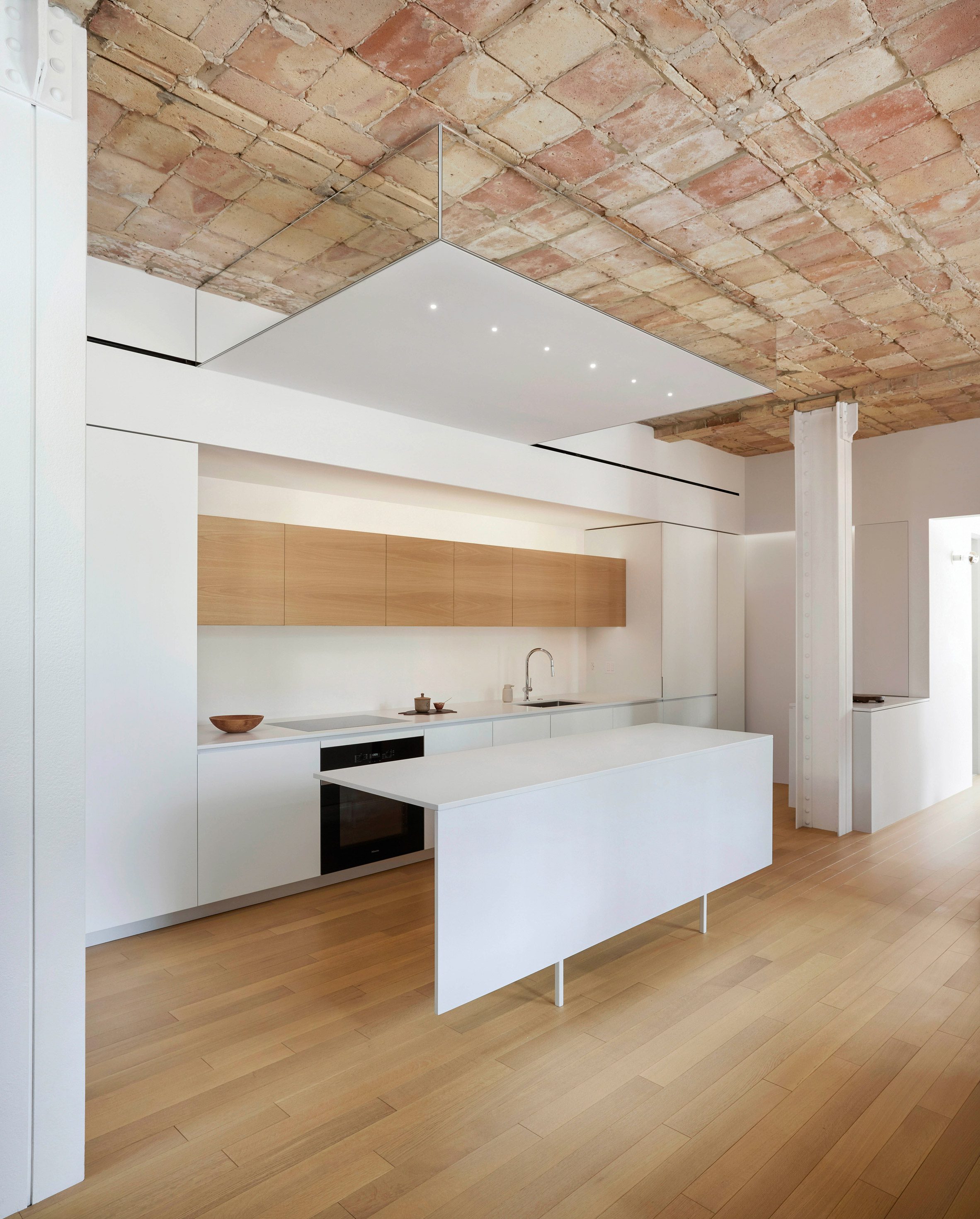 A minimalist kitchen with a mirrored soffit above a thin white island