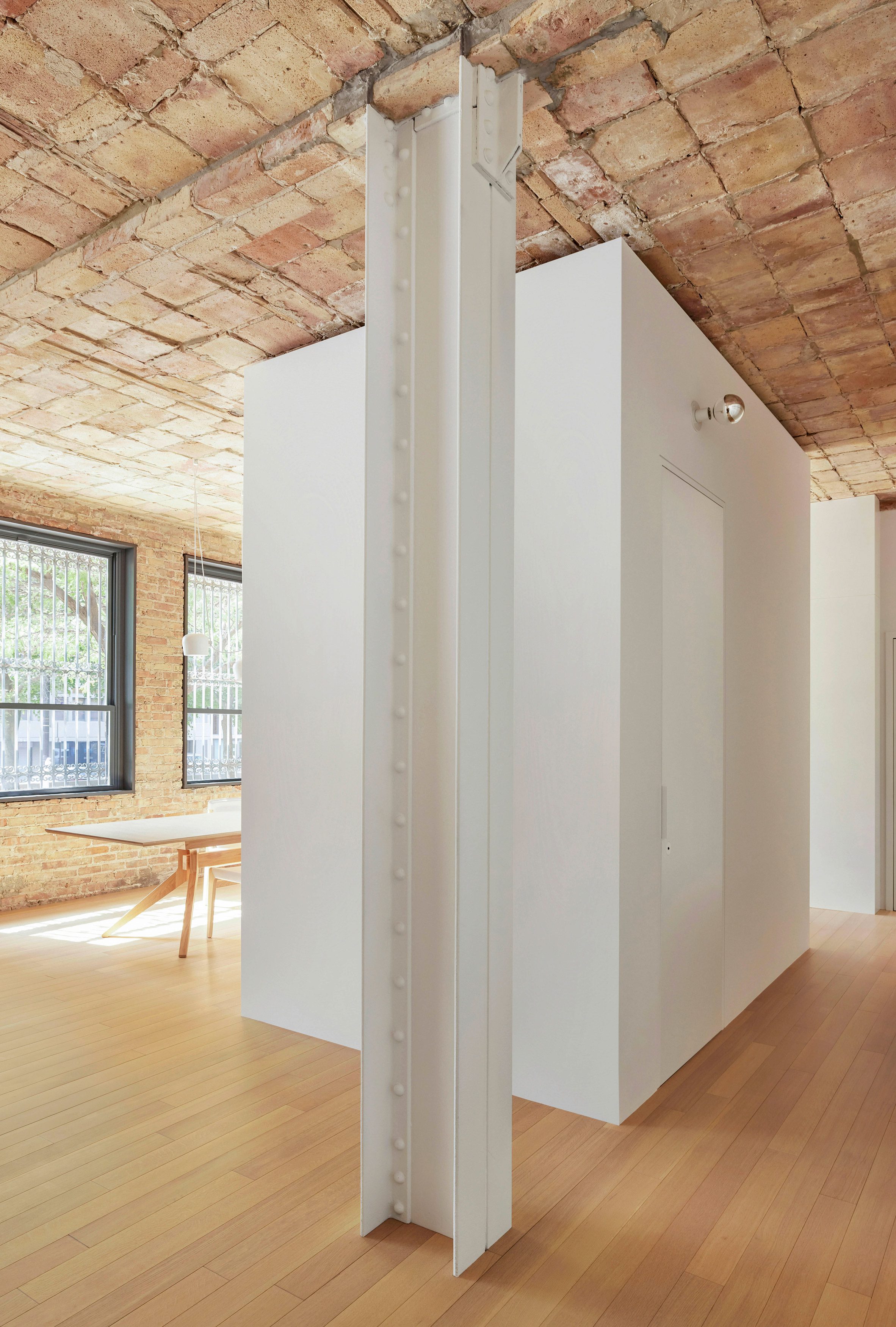 A white volume containing a bathroom divides an entryway from a dining area