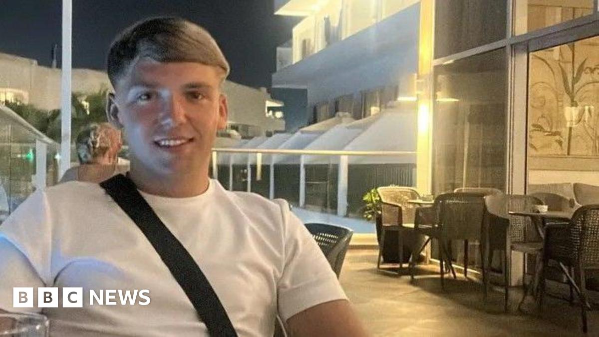 Nathan sitting in a pub with a drink. He is wearing a blue tracksuit top and has his arms crossed. He has a short beard and dark brown hair.