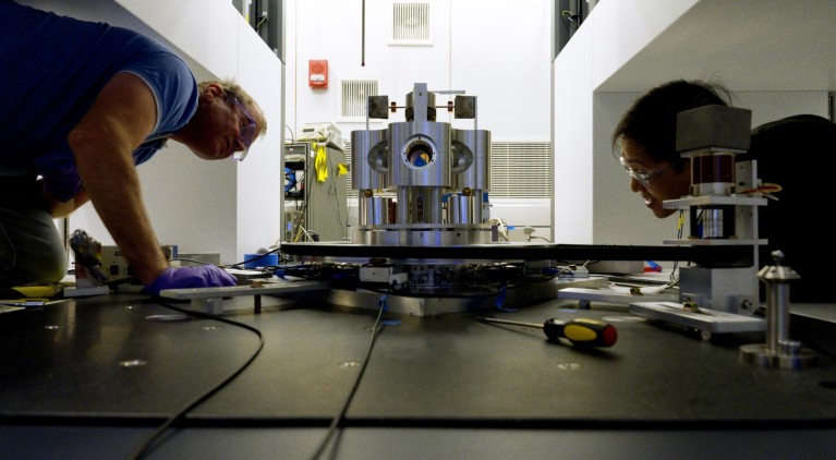 NIST scientists crouching low examine a torsion balance.