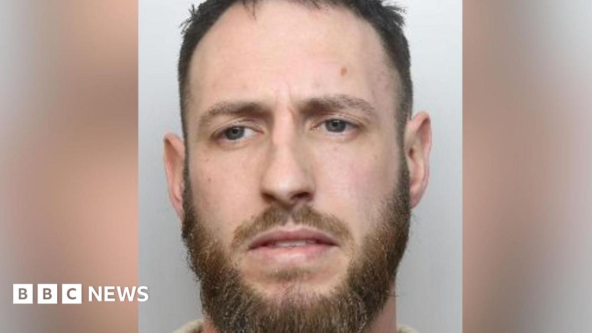 A mugshot of a man with blue eyes, a moustache and beard