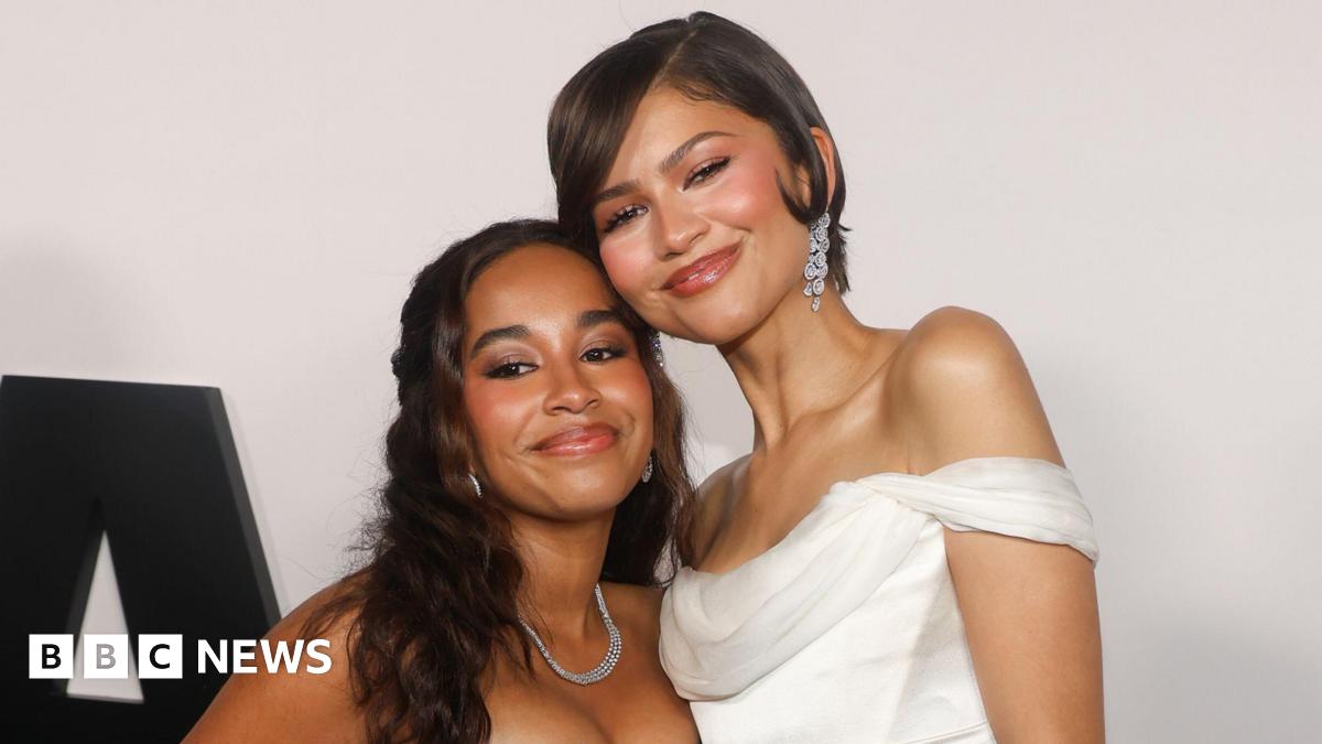 Jordyn Curet and Zendaya pose, with their faces pressed against each other. Zendaya is wearing a white off-the-shoulder dress.