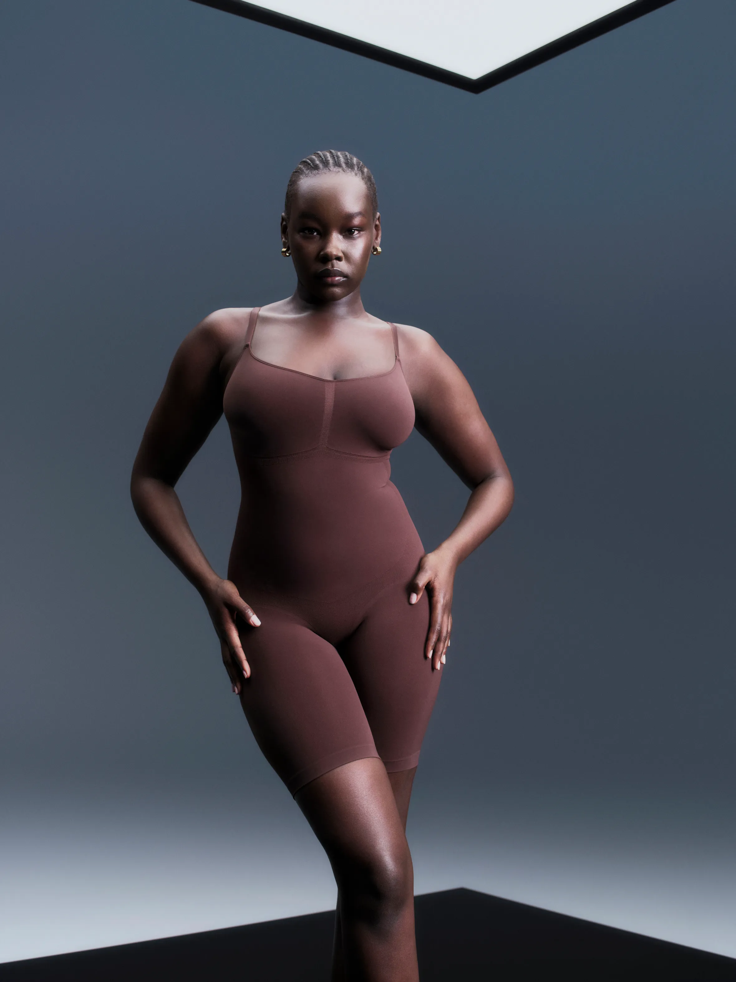 A dark-skinned model wearing a brown full body shaper.