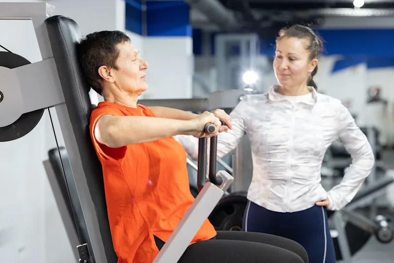 Senior woman training chest press with personal trainer