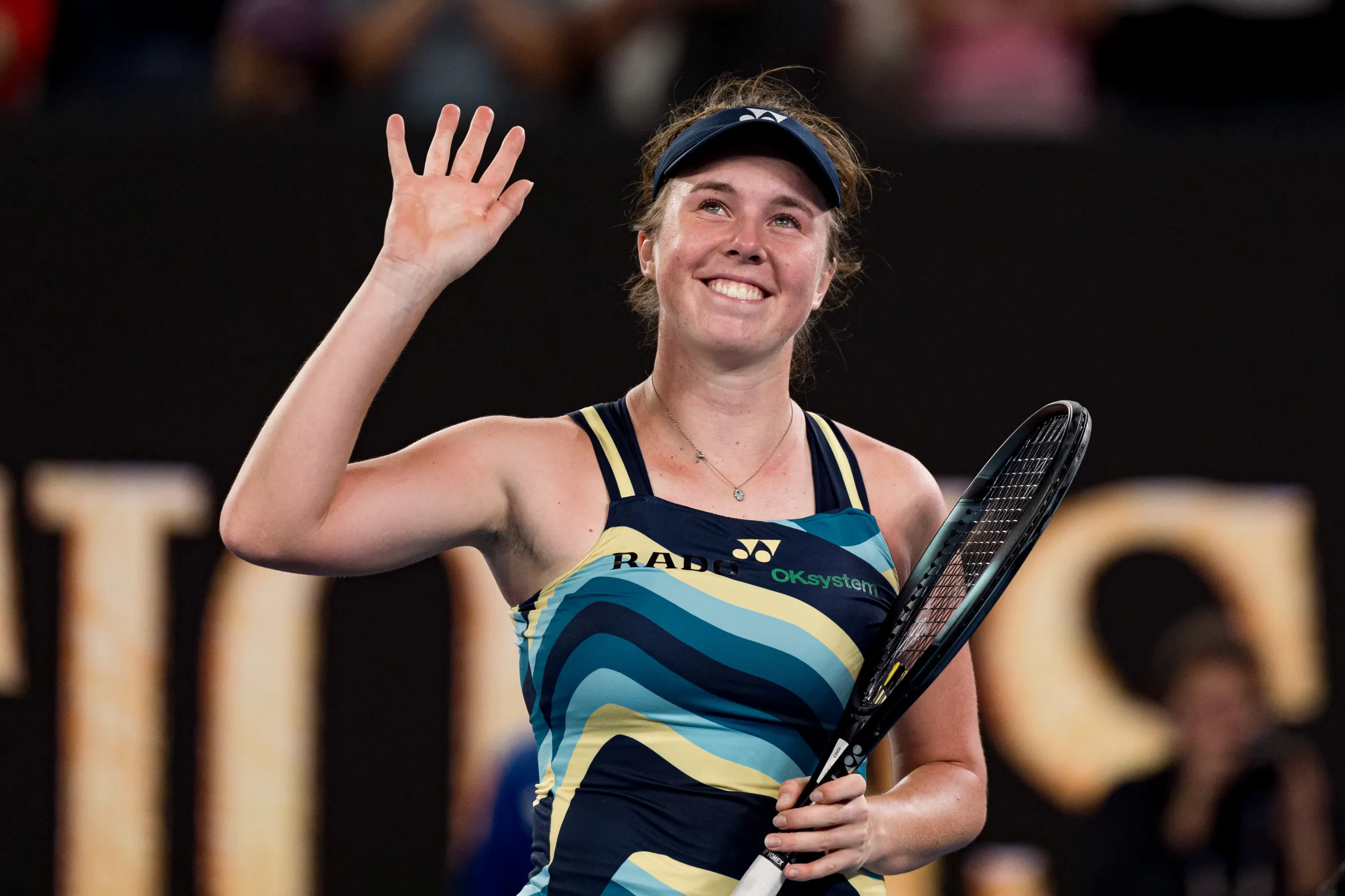 Linda Nosková waves to the crowd with a tennis racket in her other hand.