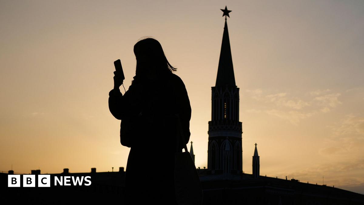 A man in a black hoodie and jeans is handing out papers to people in a queue outside an official building near the Kremlin.
