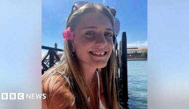 A smiling close up of a young woman with long brown hair and flowers in her hair