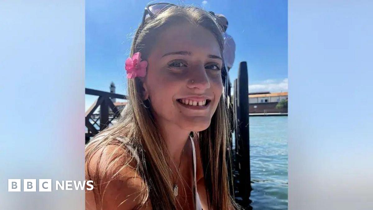 A smiling close up of a young woman with long brown hair and flowers in her hair