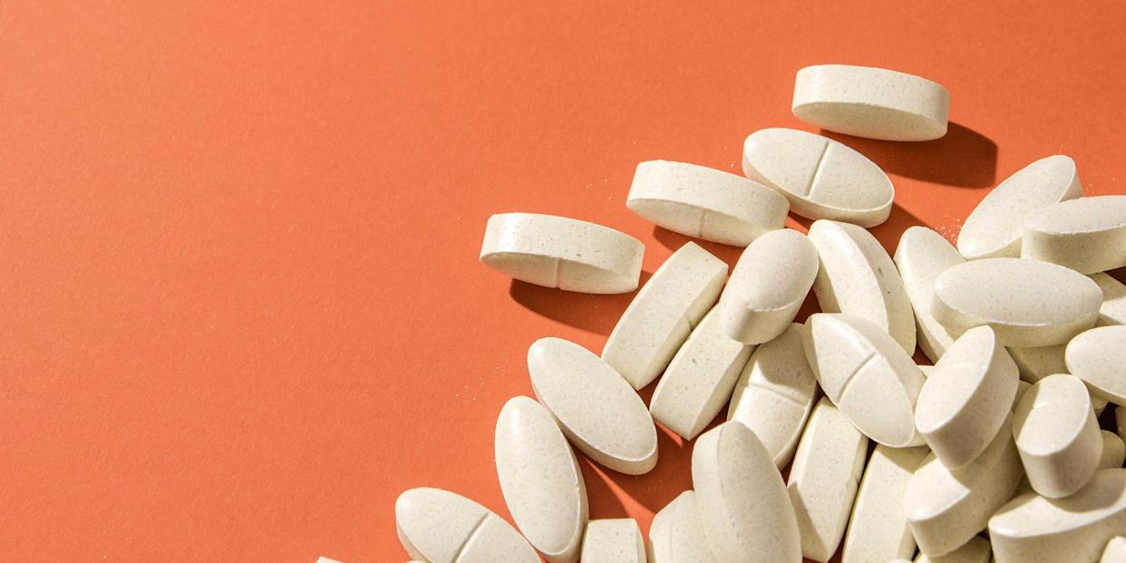 white oval pills scattered on a bright orange surface, highlighting health, medicine, and wellness concepts