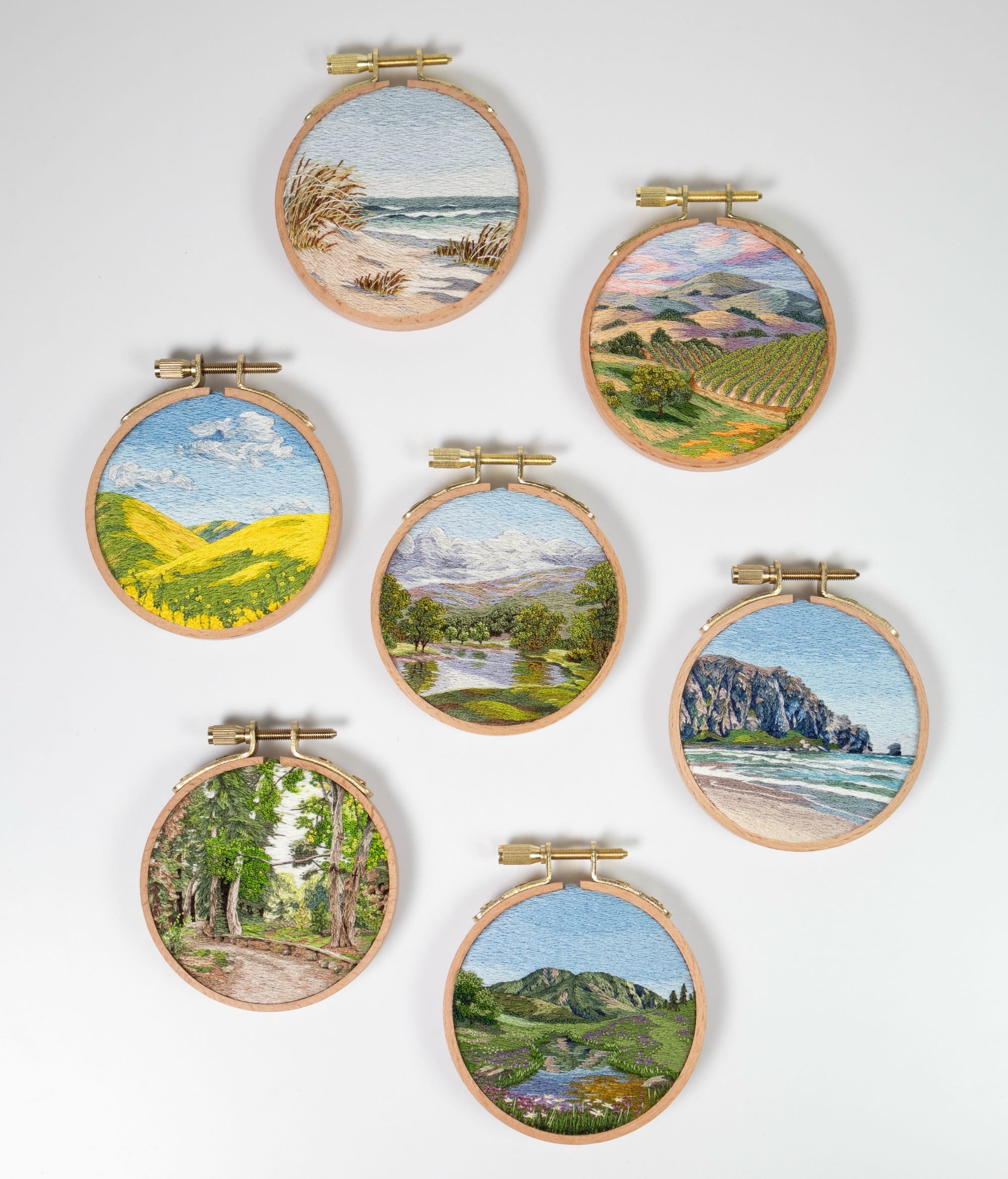 a collection of lush landscape embroideries in light wood hoops by Cassandra Dias