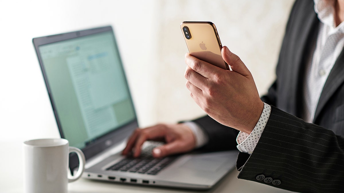 Person holding a smartphone while using a laptop