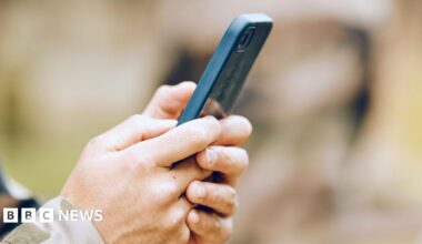 A pair of hands holding a mobile phone, with a camouflage cuff showing. This is a stock image showing a model.