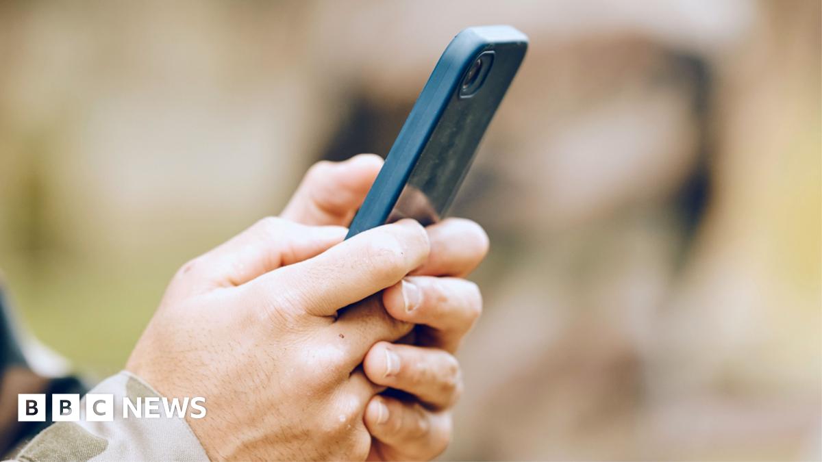 A pair of hands holding a mobile phone, with a camouflage cuff showing. This is a stock image showing a model.