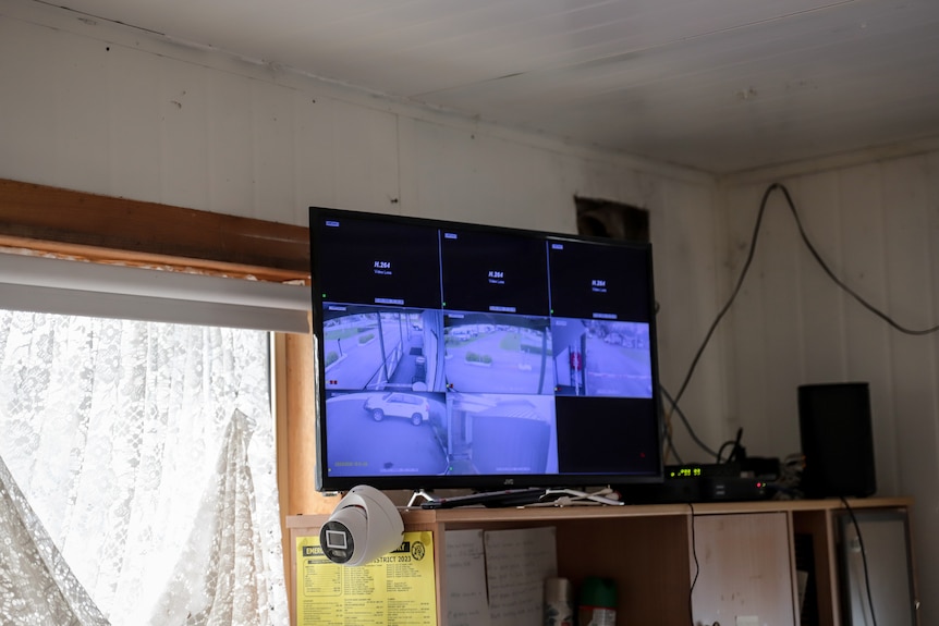 A television screen perched in a corner of a room displays grainy black and white CCTV images, a security camera sits below.