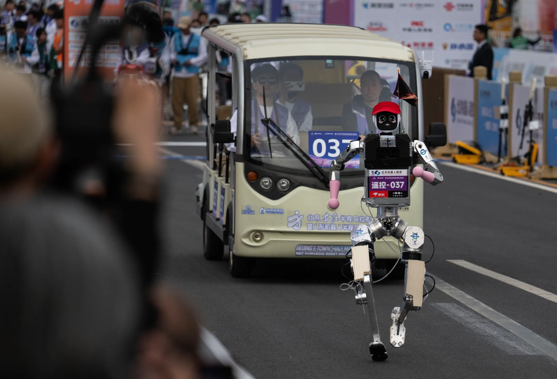 A humanoid robot with a red hat runs on a track during the Beijing Humanoid Half Marathon.