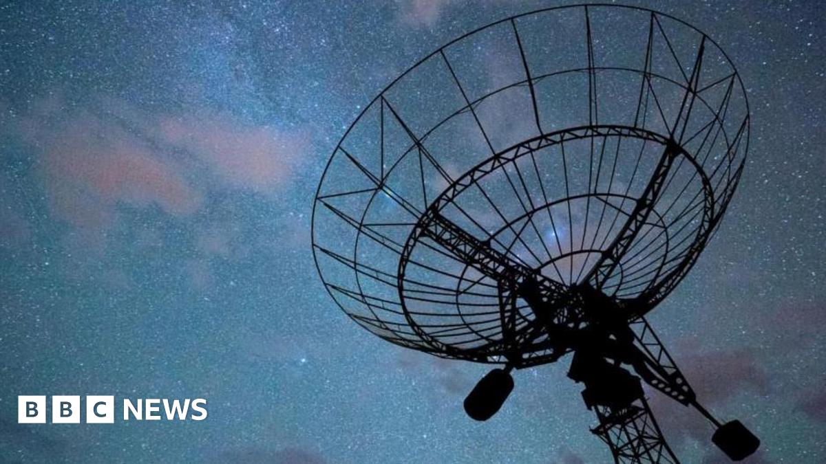 A radar disc pointed a dark night sky with an array of stars and clouds, tinged in purple, visible. The radar itself is in silhouette.