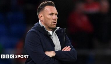 Craig Bellamy, in an open dark jacket with a grey top underneath, looks on with a focused stare during Wales' match against Northern Ireland