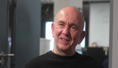 Peter Molyneux is sitting in his office looking off camera during an interview, wearing a black jumper