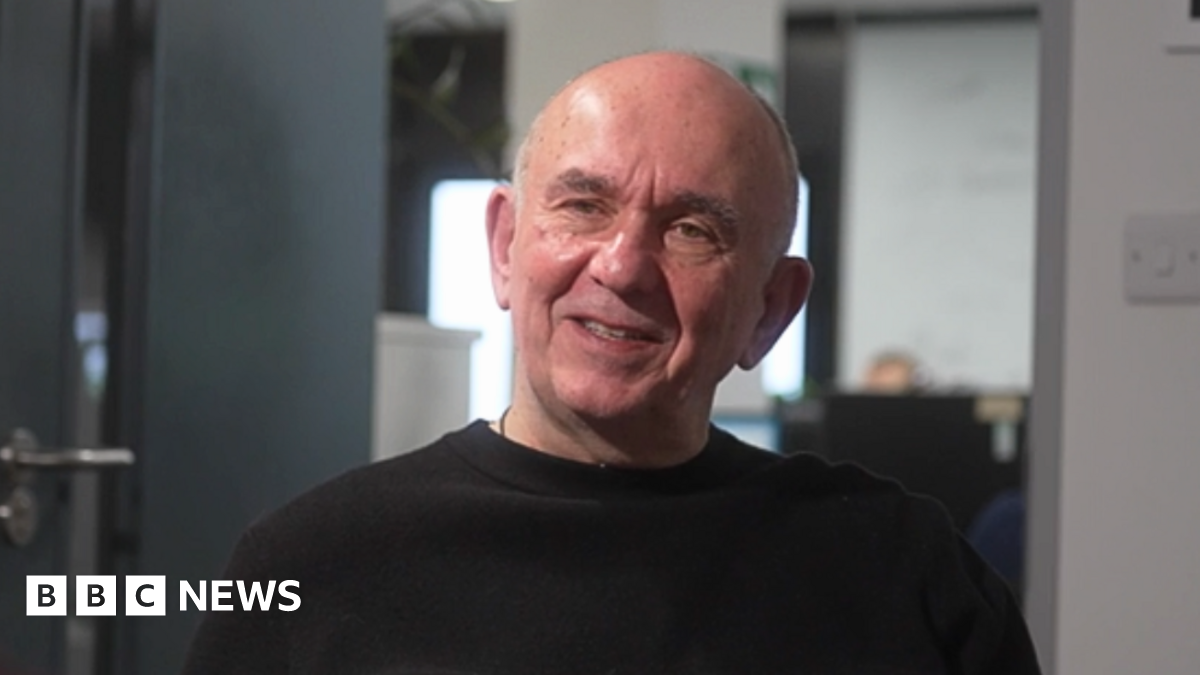 Peter Molyneux is sitting in his office looking off camera during an interview, wearing a black jumper