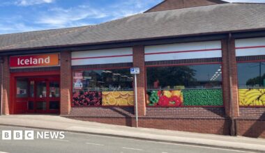 A shopfront with pictures of fruit in the window and an orange and red signage which reads "Iceland"