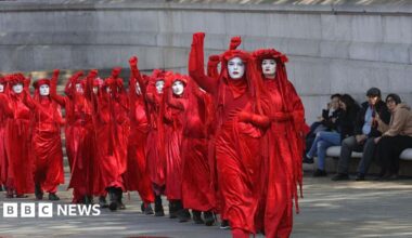 A line of women dress in red, each with a fist raised, protest in London against new oil and gas fields
