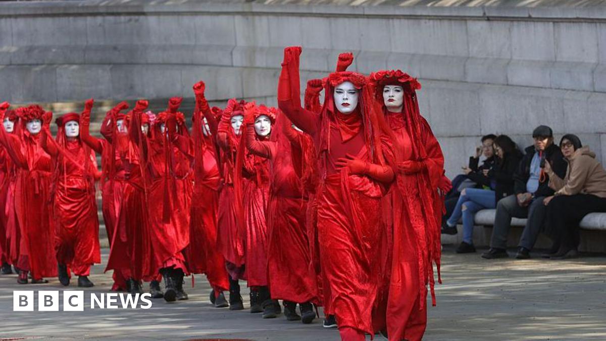 A line of women dress in red, each with a fist raised, protest in London against new oil and gas fields
