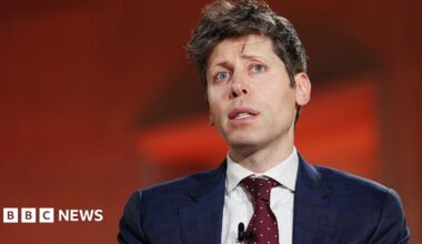 Sam Altman against red background, wearing blue suit and red tie with white dots, looks up and to the side