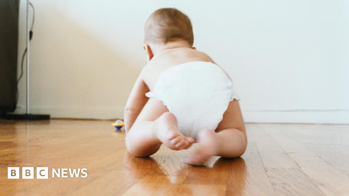 A baby crawling on a wooden floor