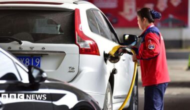 A female petrol station attendant refuels a white car