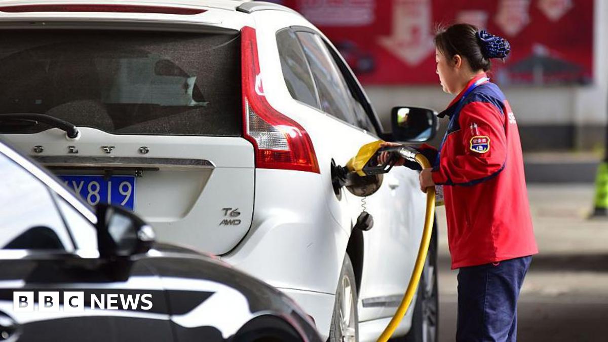 A female petrol station attendant refuels a white car