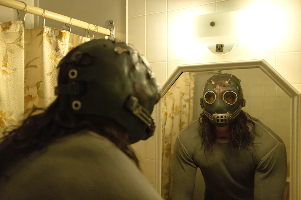 James Preston Rogers stands before a bathroom mirror wearing a frightening leather mask in a scene from Psycho Killer.