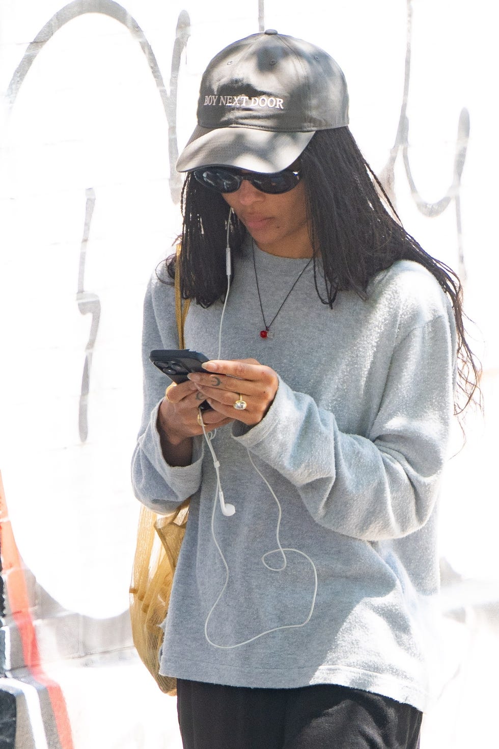 Person wearing a gray sweater and a cap, using a mobile device.