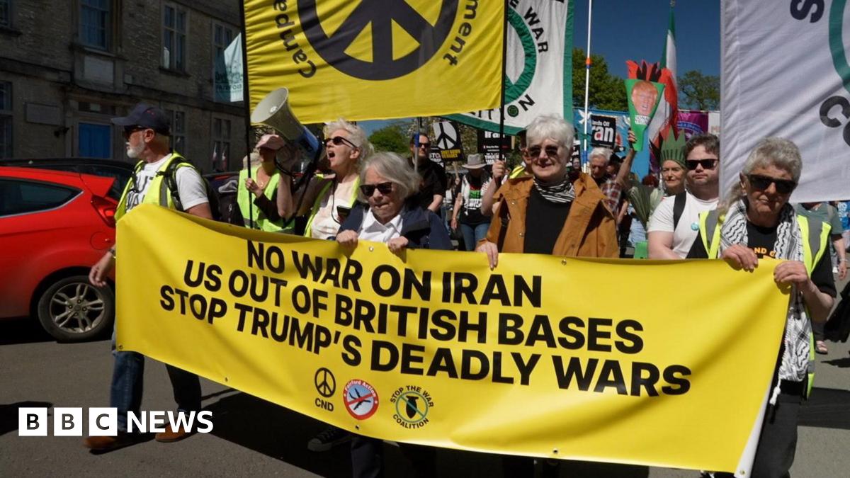 Protesters at the front of a demonstration are holding a large yellow anti-war banner, with many people following behind them.