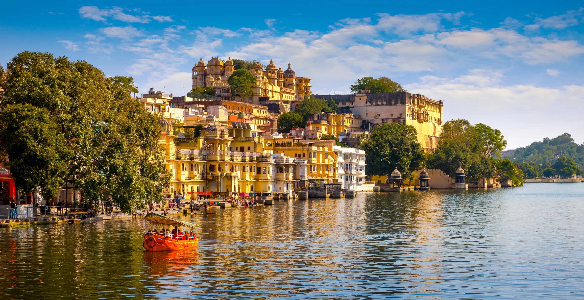 The City Palace and Pichola Lake in Udaipur, India, with a boat on the water.