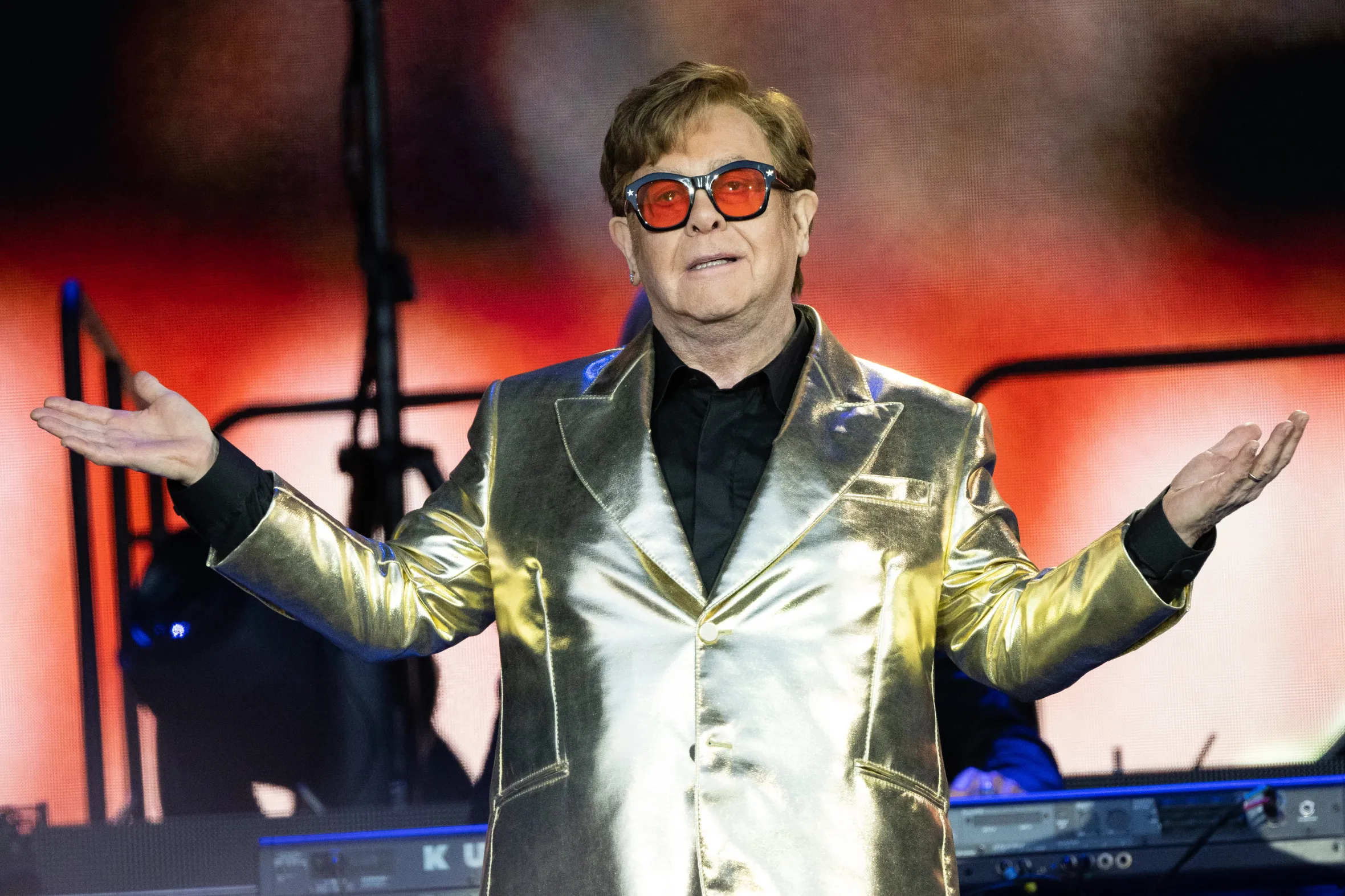 Elton John in a gold suit and red-tinted glasses performs on the Pyramid Stage at Glastonbury Festival 2023.