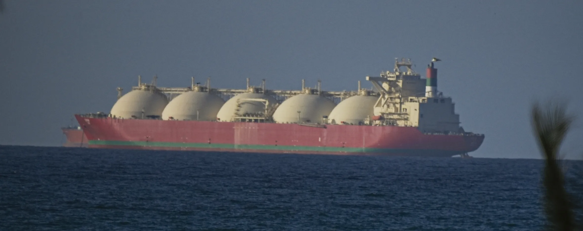 Red and green LNG tanker with five large white spherical tanks sailing in the Strait of Hormuz.