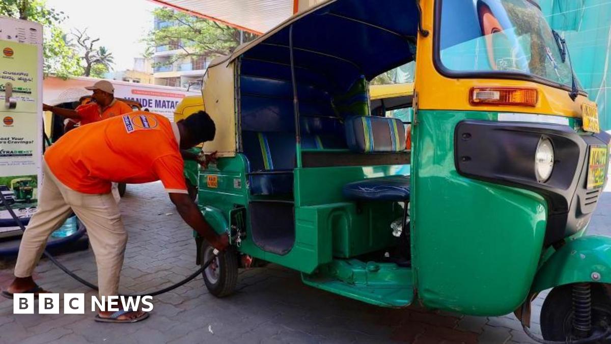 A petrol station attendant helps a customer top up his auto rickshaw in India