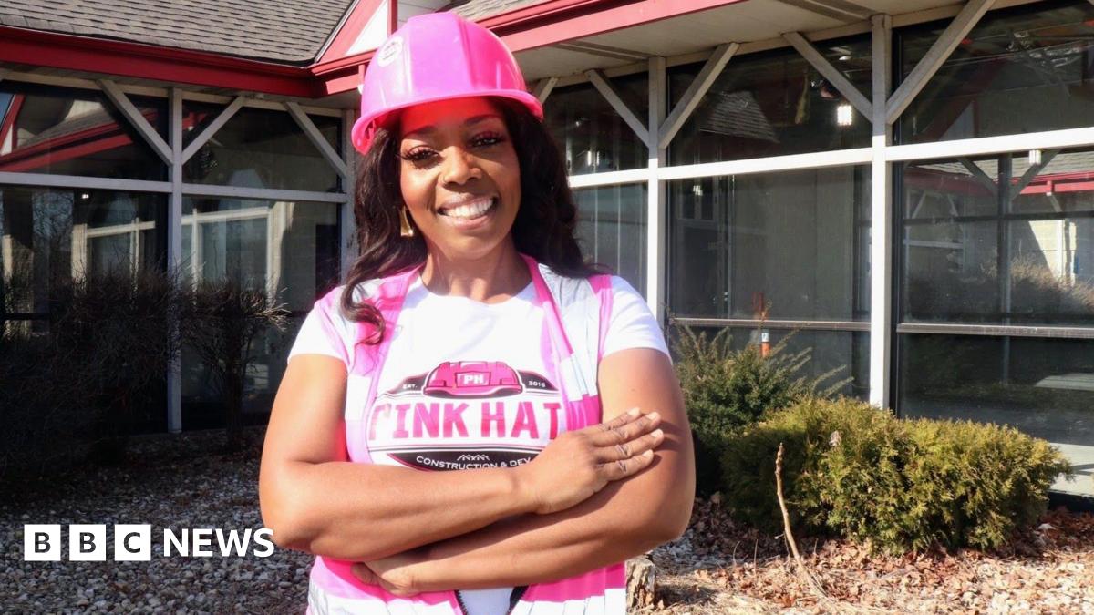 Business owner Traci Quinn smiles at the camera while wearing a pink hard hat and pink striped top